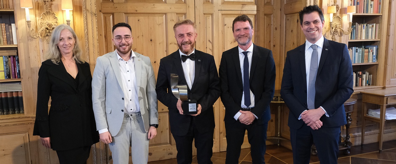 Foto von Herrn Göksel als Gewinner des Mazda-Awards und anderen Personen in einem schicken Foyer. Alle tragen elegante, förmliche Kleidung.